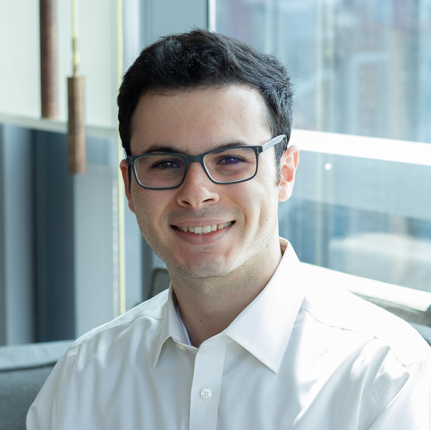 A white man with short black hair and glasses smiling in the sun