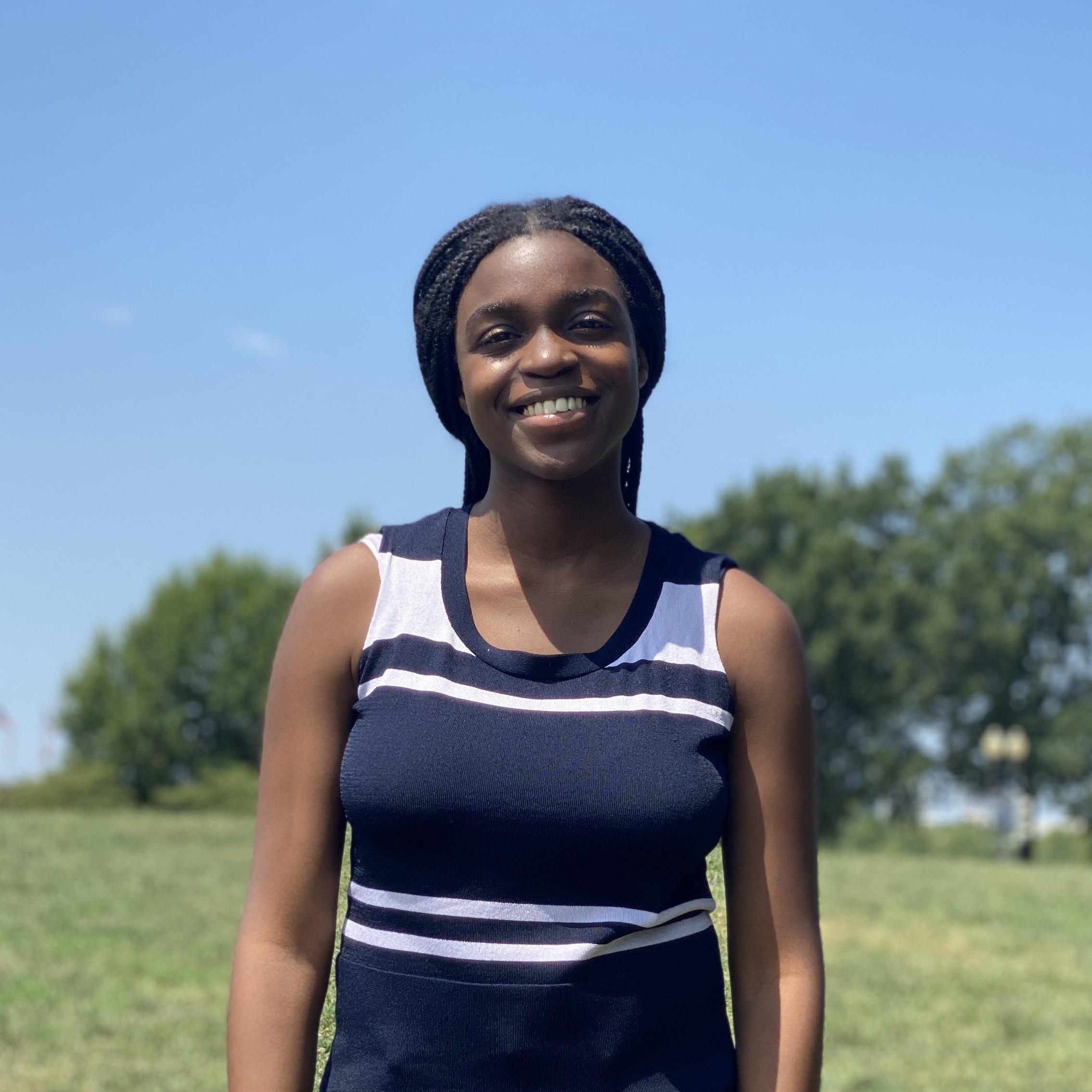 A black woman smiling and wearing a blue striped shirt outside on a sunny day