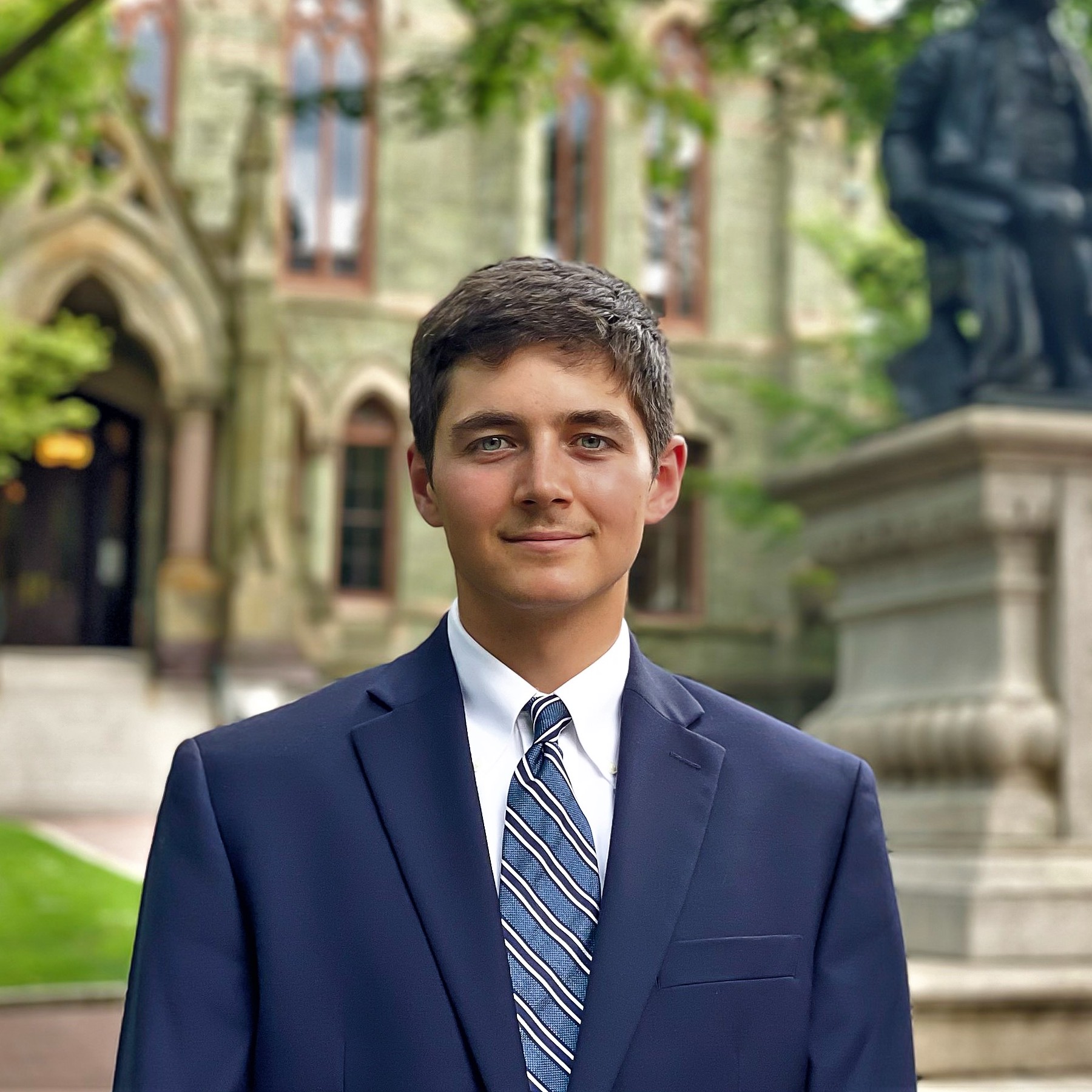 A man in a suit and tie before an academic building