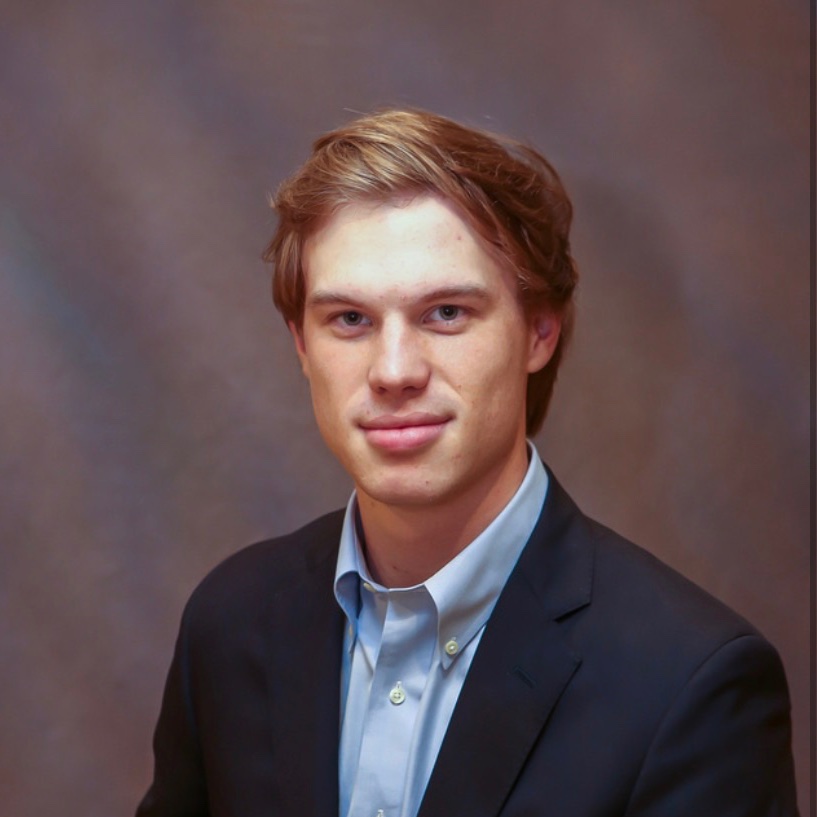 A white man with blond hair in a suit before a grey backdrop