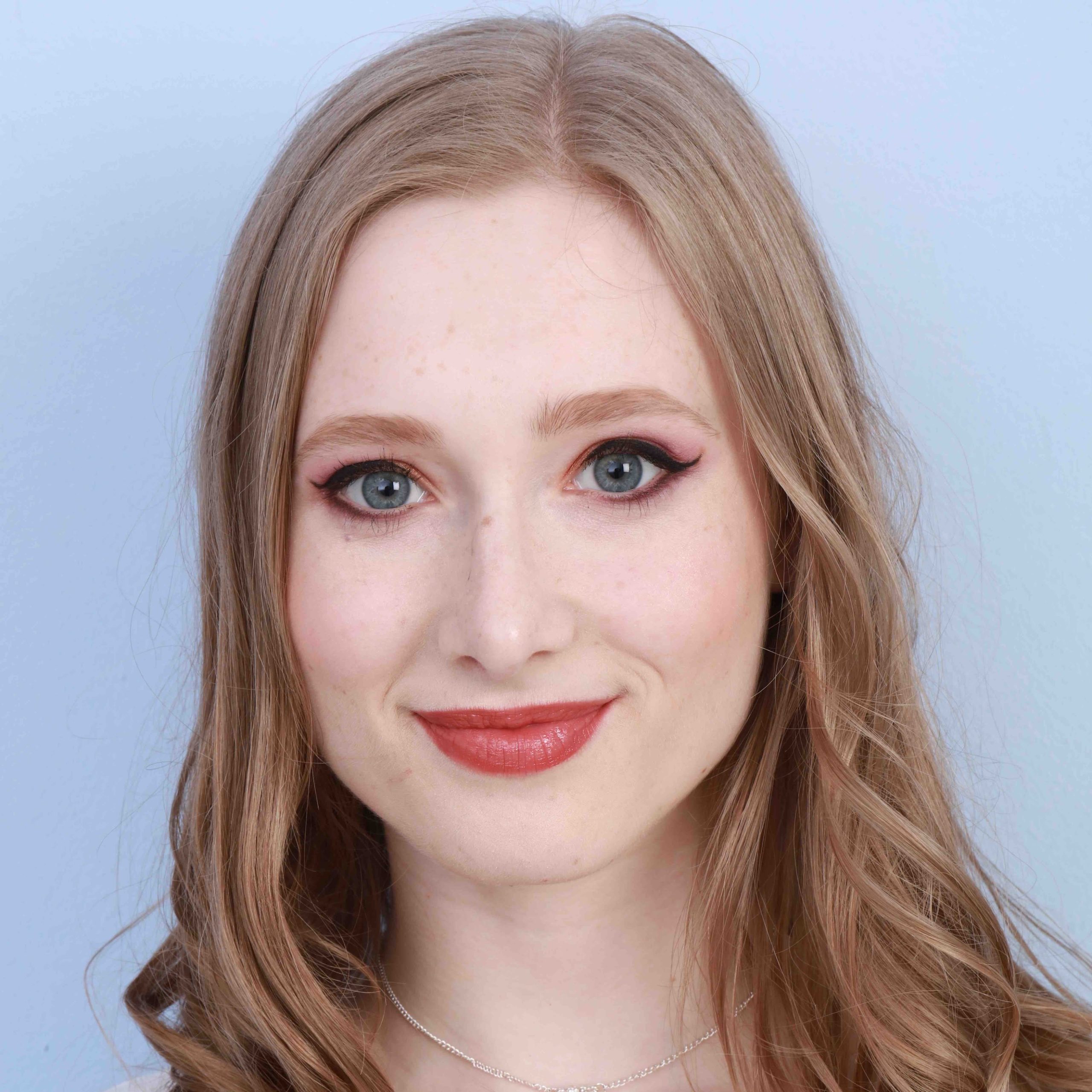 A woman smiling with blonde hair and red lipstick before a blue background