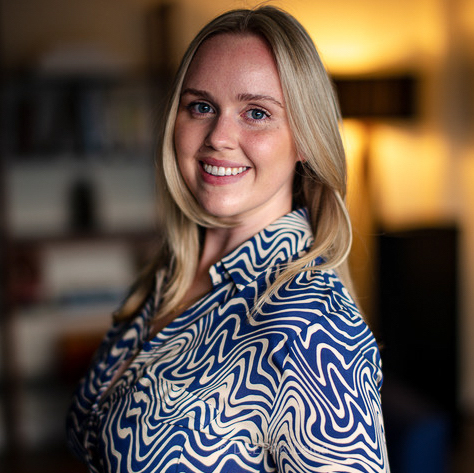 Smiling woman with blonde hair wearing a blouse with a bright blue pattern