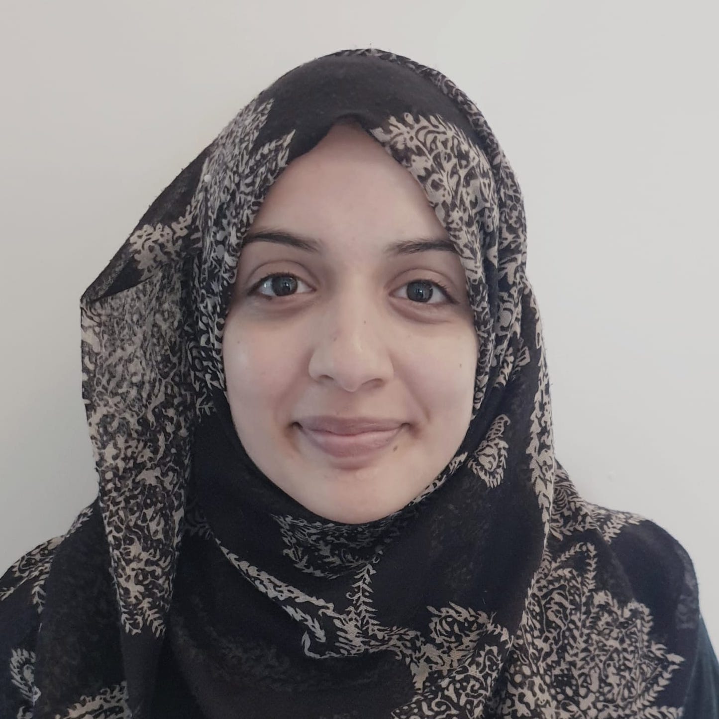 Woman of color wearing a head scarf smiling before a grey background