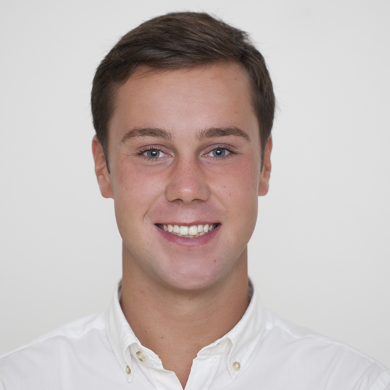 A white man with short brown hair smiling wearing a white collared shirt