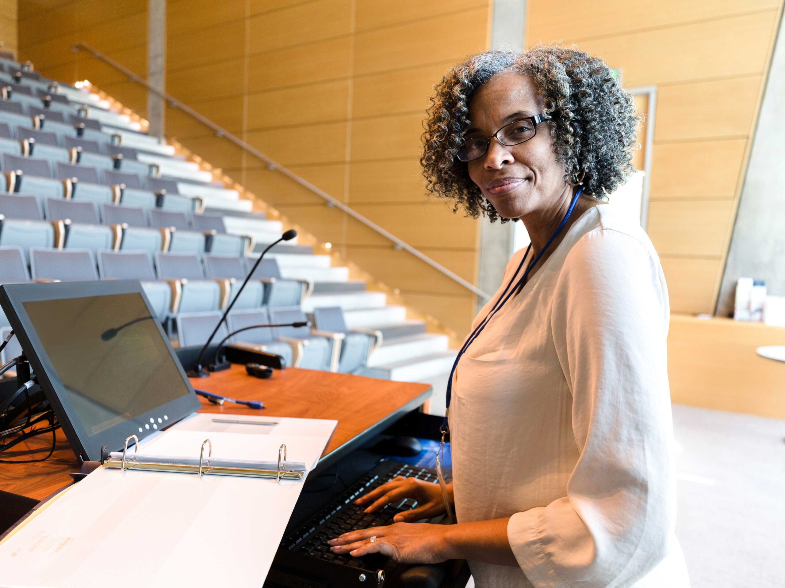 professor sits in a university lecture hall writing on a computer