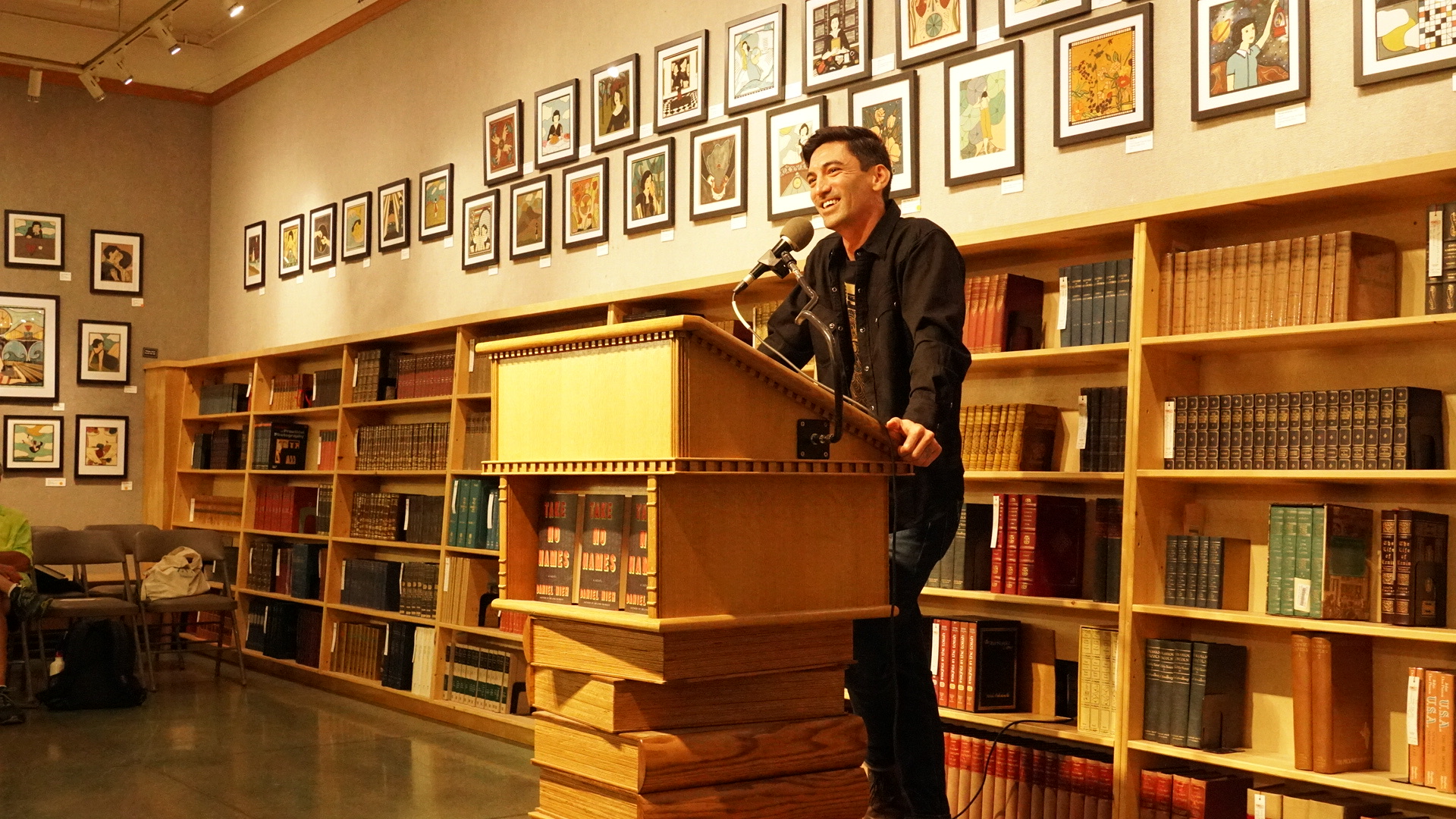 Daniel Nieh stands at a podium during a bookstore event for his novel Take No Names