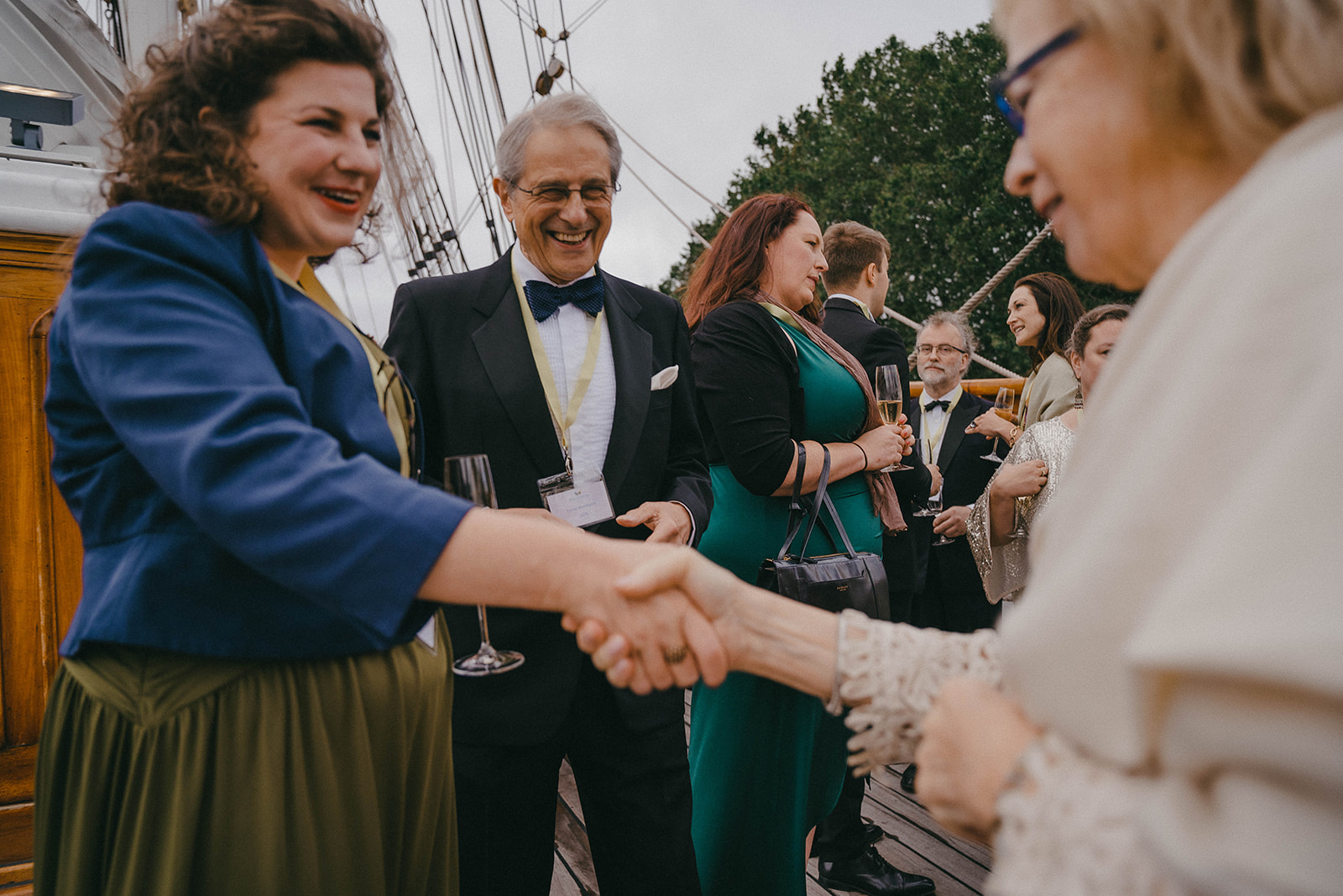 Alumni meet and shake hands over champagne on the deck of the Cutty Sark.