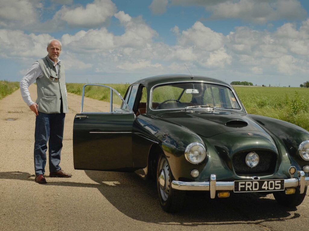 Justin stands alongside his 1956 Bristol 405, Frieda, on a road in the English countryside.