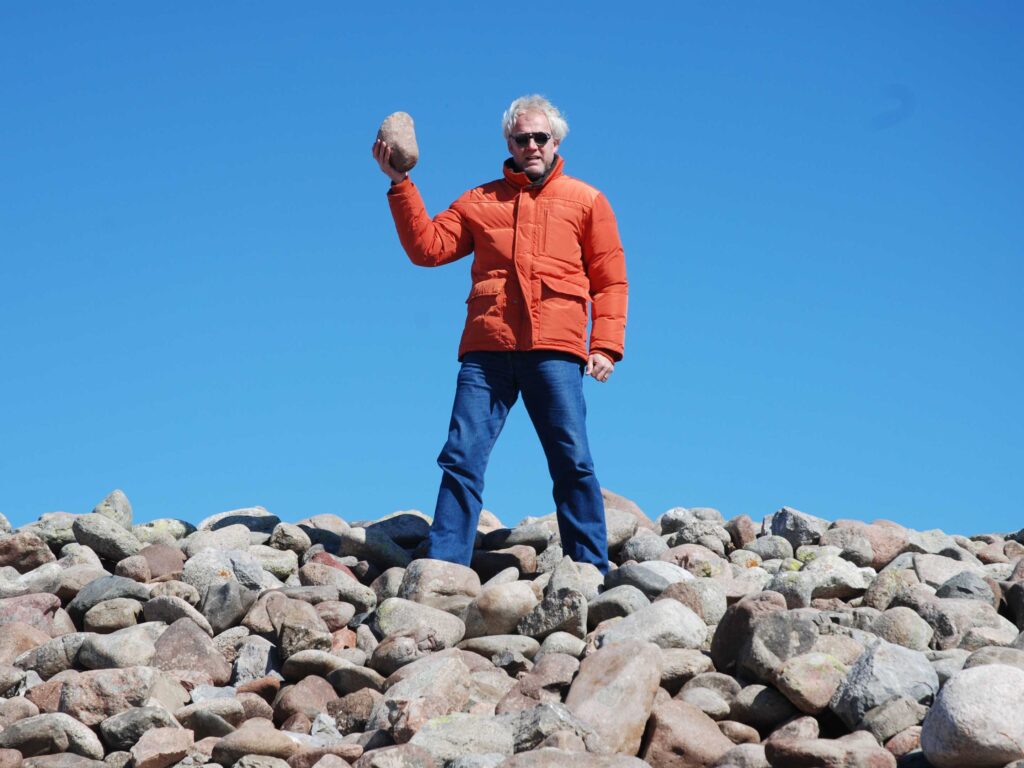 Justin stands on a mound lifting up a rock while traveling through Kyrgyzstan.