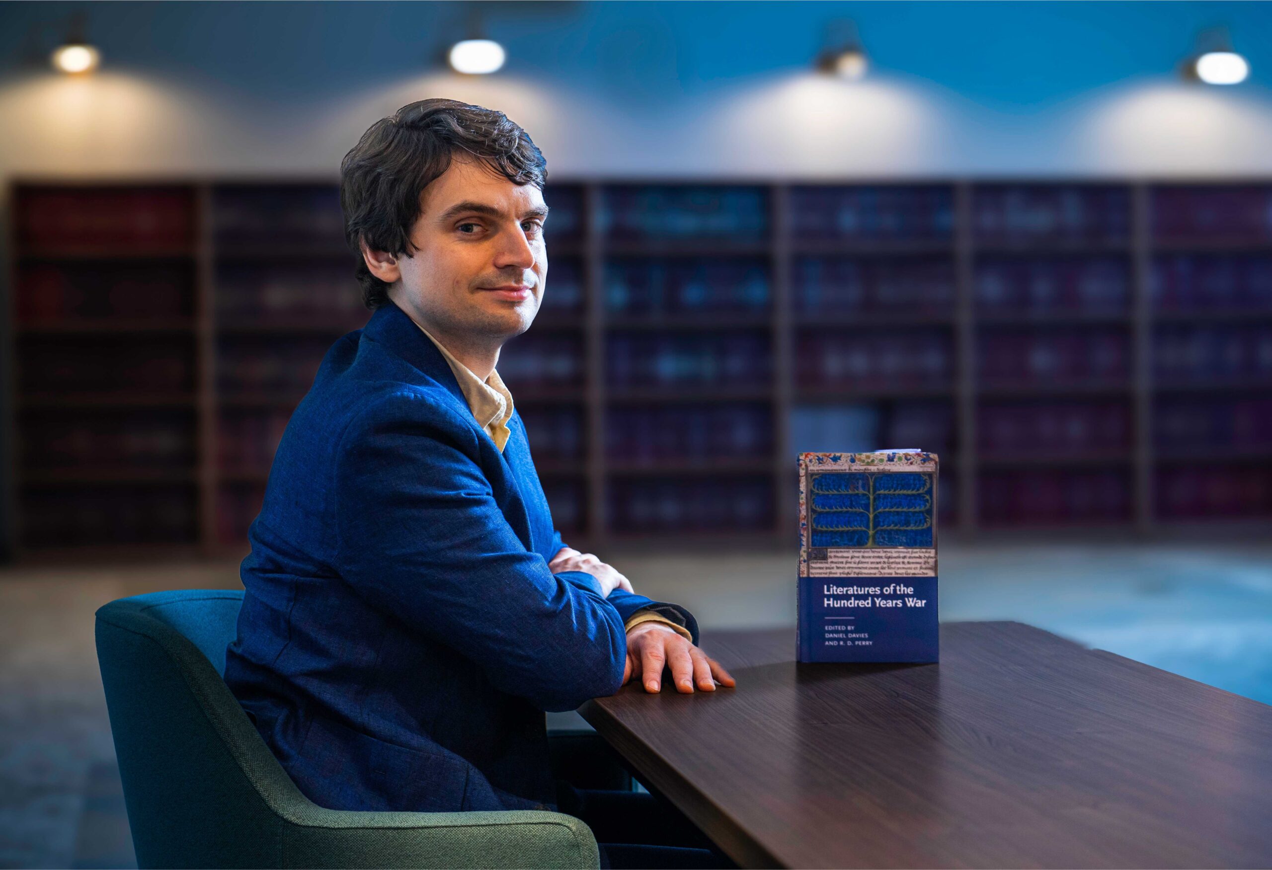 Daniel sits in a library with his collection of essays Literatures of the Hundred Years War